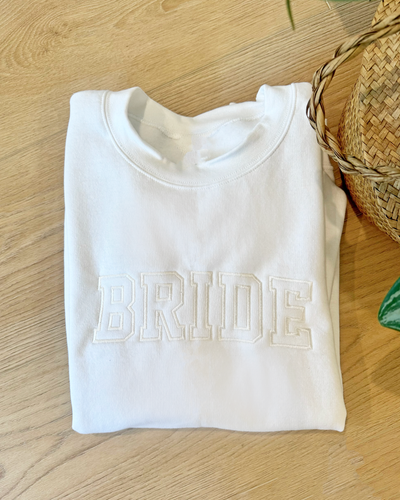 A women's embroidered crewneck sweatshirt with the word "Bride" elegantly stitched on the front. This soft and comfortable white sweatshirt is perfect for the bride-to-be as she prepares for her big day. Available in unisex sizes Small to Extra Large, made from a preshrunk 50/50 cotton and polyester blend.